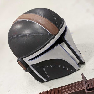 May include: A black and white helmet with a brown stripe and stitching details. The helmet has a visor and is made of a hard material.