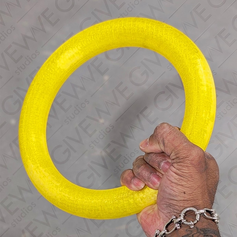 Puede incluir: Un anillo de ejercicio amarillo brillante hecho de goma. El anillo es grueso y tiene una superficie texturizada.