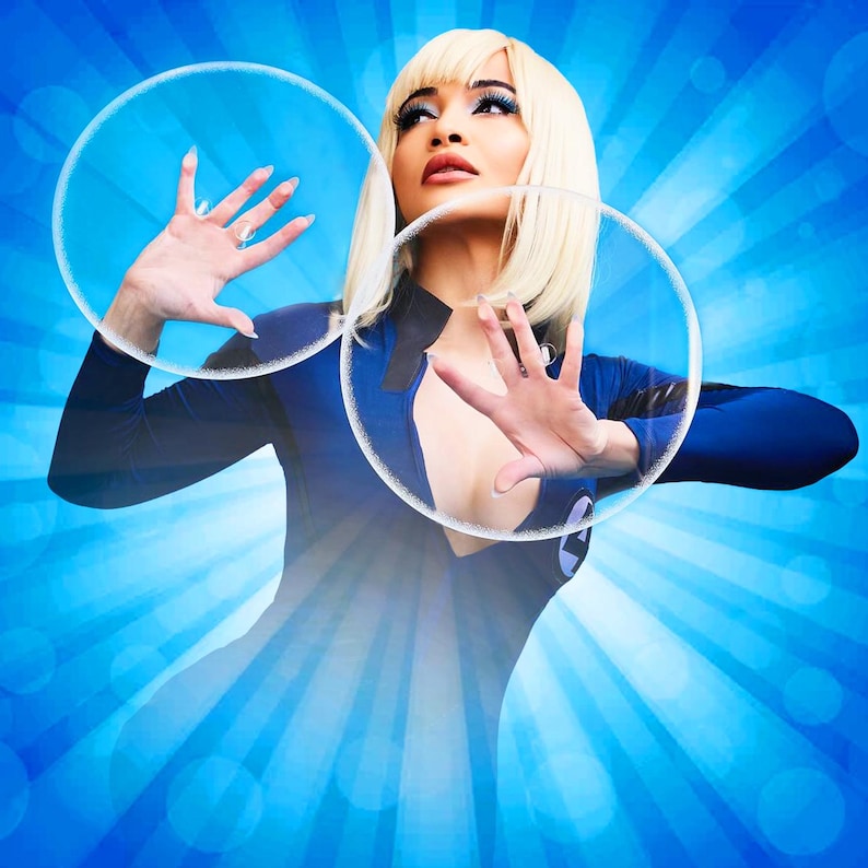 May include: A woman with blonde hair wearing a blue jumpsuit stands in front of a blue and white background with two large clear circles around her.