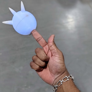 May include: A hand wearing a silver chain bracelet holds a light blue, spiky, rubber ball.