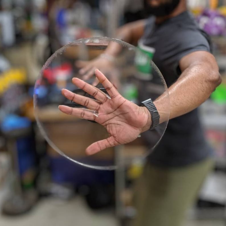 May include: A person's hand is shown through a clear, round, plastic disc. The disc is held in front of the person's body.