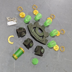 May include: A green and black eye-shaped game piece with gold rings and green glass vials. The game piece is surrounded by gold rings and green glass vials.