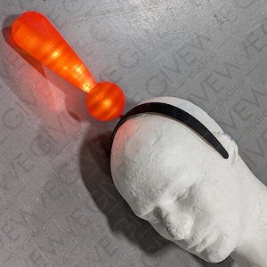 May include: A red exclamation point headband with a black elastic band. The exclamation point is lit up with a warm orange glow.