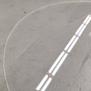 May include: A clear acrylic round table top with a decorative design of three parallel lines.
