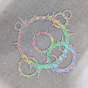 May include: A silver, iridescent, decorative metal design with a circular shape and multiple interlocking gears. The design has a rainbow-like sheen.