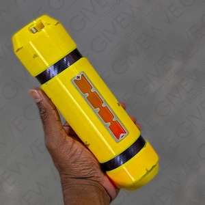 May include: A yellow cylindrical object with a black and silver stripe around the middle. The object has a rectangular orange and silver panel with a pattern on it.
