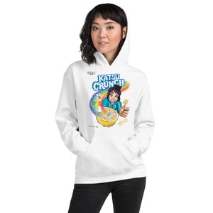 May include: White hoodie featuring a colorful graphic of a cartoon character and the text "KATSU CRUNCH". The graphic includes a rainbow, cereal bowl, and the words "sugar is tasty, sometimes". The hoodie has a front pocket and a hood.