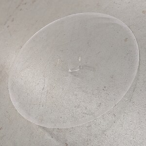 May include: A clear plastic cake stand with a raised edge. The stand has a small, clear plastic handle in the center.