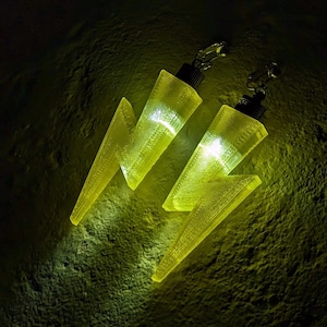May include: A pair of yellow lightning bolt shaped earrings with clear lights inside. The earrings are made of a translucent plastic material.