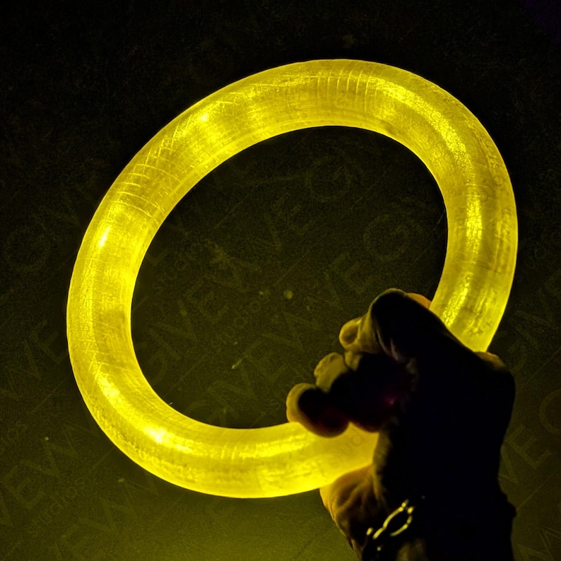 Puede incluir: Un anillo brillante de color amarillo, hecho de material flexible, est&aacute; siendo sostenido por una mano.