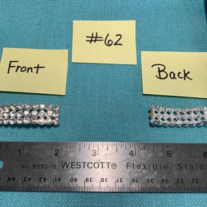 May include: A close-up of two silver-colored rhinestone embellishments, one labeled "Front" and the other "Back". The front piece is approximately 2 inches long. The background is a light blue surface.