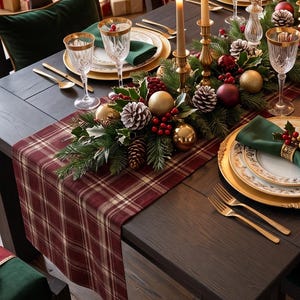 May include: A dark wood dining table set for a holiday meal with white plates, gold-rimmed glassware, and green cloth napkins. A centerpiece of pine branches, pinecones, red berries, gold ornaments, and tall taper candles runs down the center.