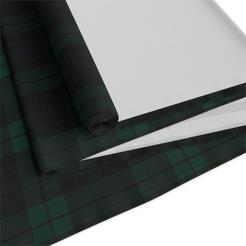 May include: A fabric roll featuring a dark green and black plaid tartan pattern. The material is partially unrolled, revealing a solid white underside. The textile displays a consistent grid of intersecting dark lines and deep green blocks.