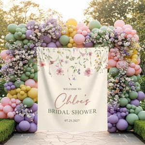 Pu&ograve; includere: Un banner color crema con dettagli floreali e la scritta "Welcome to Chloe's Bridal Shower" e la data 07.25.2027. Il banner &egrave; incorniciato da un arco di palloncini colorati. L'arco &egrave; fatto di palloncini dai colori pastello.