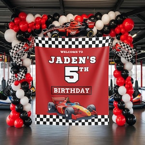 May include: A red birthday backdrop featuring a checkered border, a race car illustration, and the text "WELCOME TO JADEN'S 5TH BIRTHDAY". The banner is framed by an arch of red, white, and black balloons, with a race car balloon at the top center.