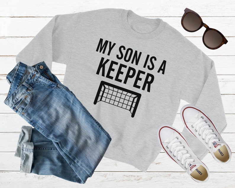 Puede incluir: Sudadera gris con el texto "Mi hijo es un portero" y una silueta negra de una porter&iacute;a de f&uacute;tbol.