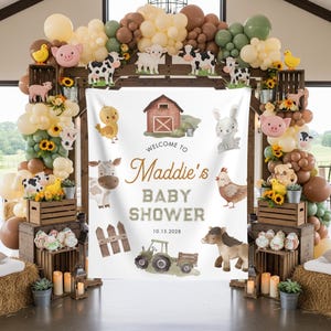 May include: A rustic baby shower backdrop with a farm theme. The banner reads "Welcome to Maddie's Baby Shower" with the date 10.15.2028. Decorations include wooden crates, balloons, and farm animal cutouts. Hay bales and candles complete the scene.