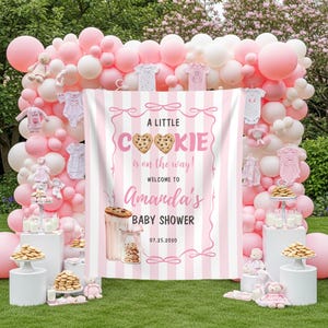 Może przedstawiać: Scena baby shower z różowymi i białymi balonami, ubrankami dla dzieci i banerem z napisem "A Little Cookie is on the way!" Witamy na baby shower Amandy, 07.25.2030. Ciasteczka i mleko są wystawione na piedestałach.