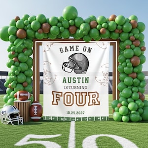 Könnte beinhalten: Fußball-Partydekoration mit einem Banner mit einem Footballhelm-Motiv und dem Text "GAME ON". Auf dem Banner steht "AUSTIN IS TURNING FOUR 10.25.2027". Grüne und braune Luftballons umrahmen das Banner. Ein Football und ein Helm liegen auf dem Boden.
