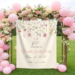 May include: A white graduation party backdrop with a floral design and the text "Welcome to Sarah's Grad Party Class of 2026 June 27 | 2026".