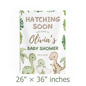 May include: A rectangular baby shower banner with the text "Hatching Soon" and "Olivia's Baby Shower." The banner features illustrations of dinosaurs and tropical leaves. The banner measures 26 x 36 inches.