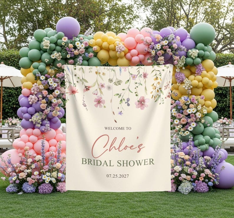 Pu&ograve; includere: Un banner per un addio al nubilato con dettagli floreali e la scritta "Welcome to Chloe's Bridal Shower 07.25.2027." Il banner &egrave; color crema ed &egrave; incorniciato da un arco di palloncini colorati e composizioni floreali.
