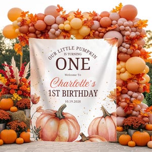 Puede incluir: Una pancarta de cumpleaños rectangular con el texto Our Little Pumpkin Is Turning One, Welcome To Charlotte's 1st Birthday y la fecha 19.10.2028. El diseño incluye calabazas estilo acuarela en la parte inferior y motas doradas sobre fondo blanco.