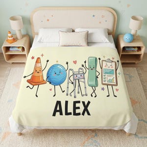 May include: A cream-colored blanket featuring a cartoon graphic of a traffic cone, a blue exercise ball, a walker, a green resistance band, and a clipboard with a chart. The name ALEX is printed in large black capital letters below the characters.