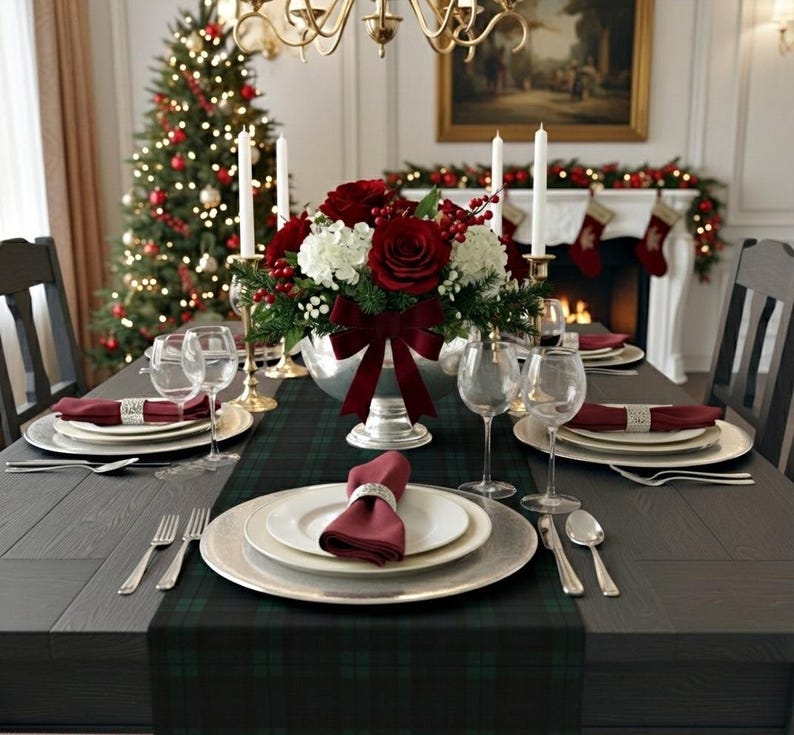 May include: A formal dining table setting featuring a dark green plaid runner, white plates, burgundy napkins with silver rings, clear wine glasses, and silver cutlery. A centerpiece of red roses, white hydrangeas, and berries sits in a silver bowl.