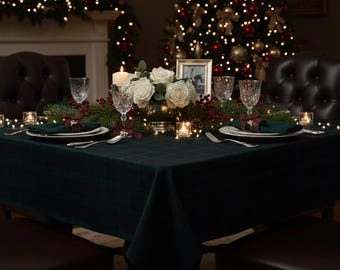 May include: A dark green plaid tablecloth covers a dining table set for a holiday meal. The table features white roses, red berries, evergreen branches, crystal glasses, dark green napkins with plaid bows, and small lit candles.