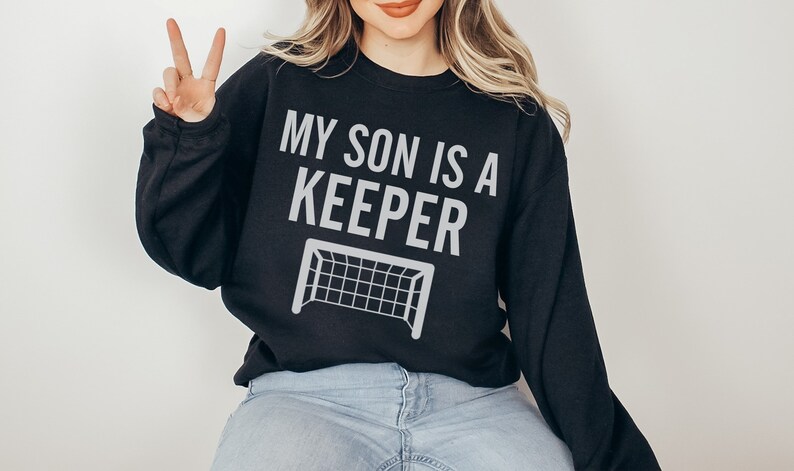 Puede incluir: Sudadera negra con el texto "MY SON IS A KEEPER" y una silueta blanca de una porter&iacute;a de f&uacute;tbol.
