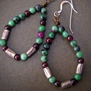 May include: A pair of green and burgundy gemstone earrings with silver hooks and brown metal beads.