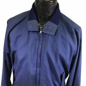 May include: A blue bomber jacket with a zipper closure and a navy blue collar. The jacket has a pocket on the left side and a ribbed navy blue waistband.