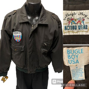 May include: A black bomber jacket with a zipper closure and two large pockets. The jacket has a patch on the left chest that says "American Sports" and a Bugle Boy Action Wear label on the right chest. The label says "Quality Tested".