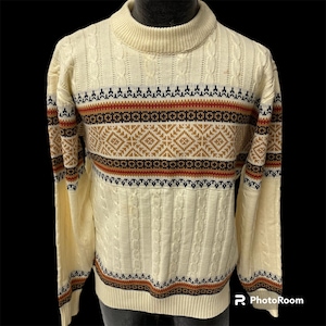 Puede incluir: Un suéter de punto de cable de color crema con un patrón geométrico marrón, rojo y negro alrededor del cuello y el dobladillo.