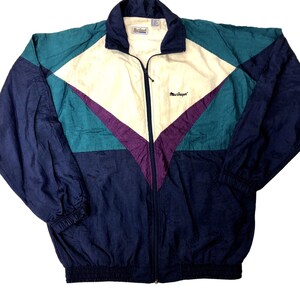 May include: A vintage windbreaker jacket in a color block design. The jacket features a navy blue, teal, cream, and purple color scheme. It has a full zipper, a collar, and the "MacGregor" logo embroidered on the chest.