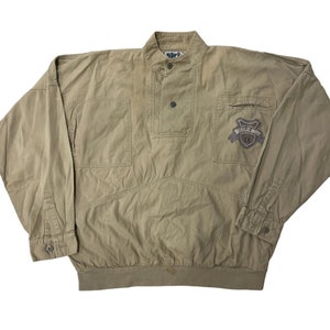 May include: A tan long-sleeve shirt with a button-up collar and a patch on the right side that says "Bugle Boy IX".