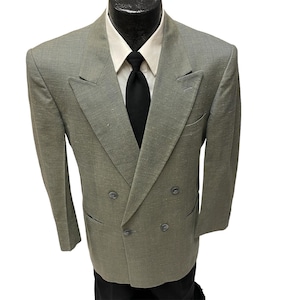 May include: A double-breasted blazer in a light gray color with a textured weave. The blazer has four buttons and two flap pockets.