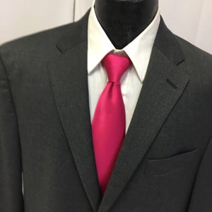 May include: A dark gray suit jacket with a white shirt and a bright pink tie.
