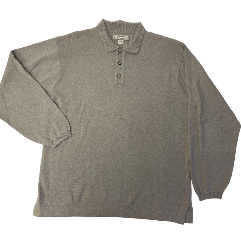 May include: A gray long-sleeve knitted polo shirt with a button-up collar and a Tommy Bahama logo.