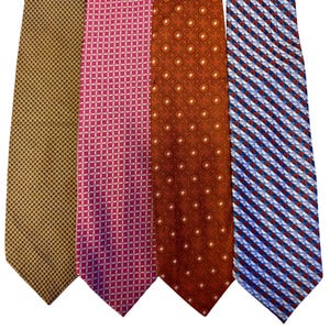 May include: Four patterned neckties. The first is gold with a small black dot design. The second is pink with a white diamond pattern. The third is rust-coloured with a white circle pattern. The fourth is blue and white with red diagonal stripes.