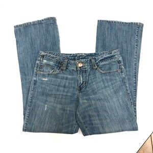 May include: A pair of blue denim jeans with a bootcut leg. The jeans have a light wash and distressed details.