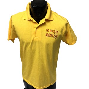 May include: Yellow short-sleeved polo shirt with an orange print that reads "DCES CLASS '63"