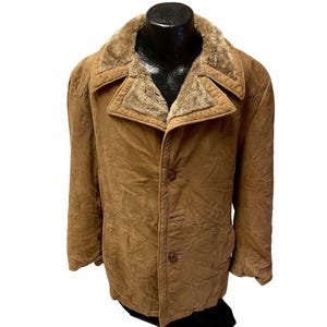 Puede incluir: Una chaqueta de ante marrón con cuello de piel sintética. La chaqueta tiene cierre de botón y dos bolsillos.