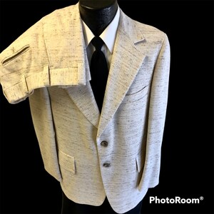 May include: A beige suit jacket with a speckled pattern. The jacket has a single breasted closure with three buttons. The jacket has two flap pockets on the front and one pocket on the left breast.