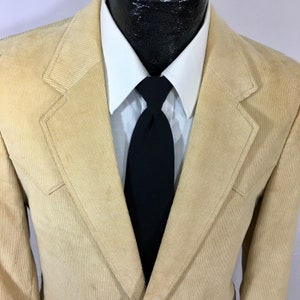 Puede incluir: Una chaqueta de pana beige con una corbata negra y una camisa blanca con cuello.