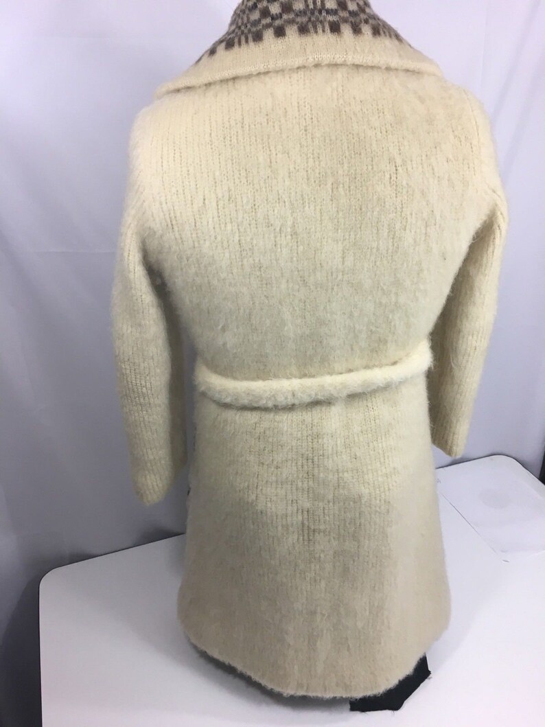 K&ouml;nnte beinhalten: Ein langer, wei&szlig;er, flauschiger Cardigan mit einem braunen und wei&szlig;en karierten Kragen und einem passenden G&uuml;rtel.