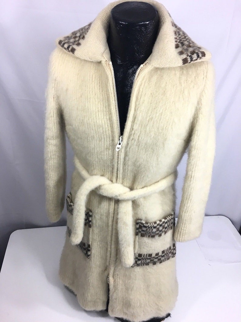K&ouml;nnte beinhalten: Ein wei&szlig;er Strickcardigan mit braunem und wei&szlig;em Muster an Kragen und Taschen. Der Cardigan hat einen Rei&szlig;verschluss und einen G&uuml;rtel.
