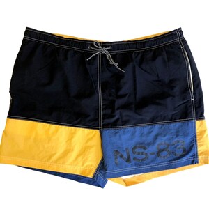 May include: Blue, yellow, and navy blue swim trunks with a white drawstring and the text "NS-83" printed on the side.