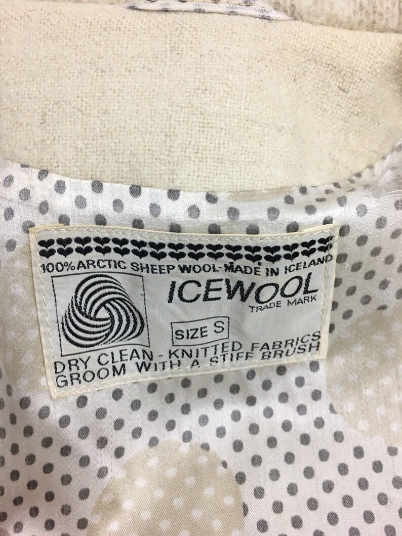 K&ouml;nnte beinhalten: Ein wei&szlig;es Etikett mit schwarzem Text und einem schwarz-wei&szlig;en Logo. Das Etikett lautet "100% Arktisches Schafwolle - Hergestellt in Island", "ICEWOOL", "Markenzeichen", "Gr&ouml;&szlig;e S", "Chemische Reinigung - Gestrickte Stoffe", und "Mit einer steifen B&uuml;rste b&uuml;rsten".